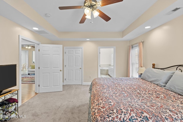 carpeted bedroom with a raised ceiling, ceiling fan, and ensuite bath