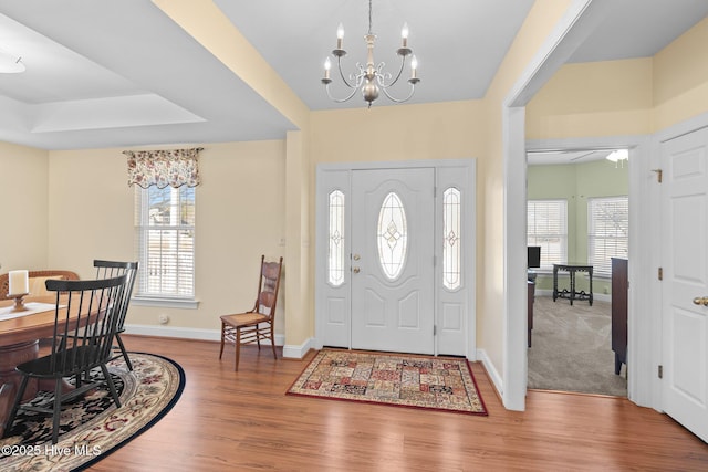 entryway featuring a healthy amount of sunlight, a tray ceiling, a notable chandelier, and wood-type flooring