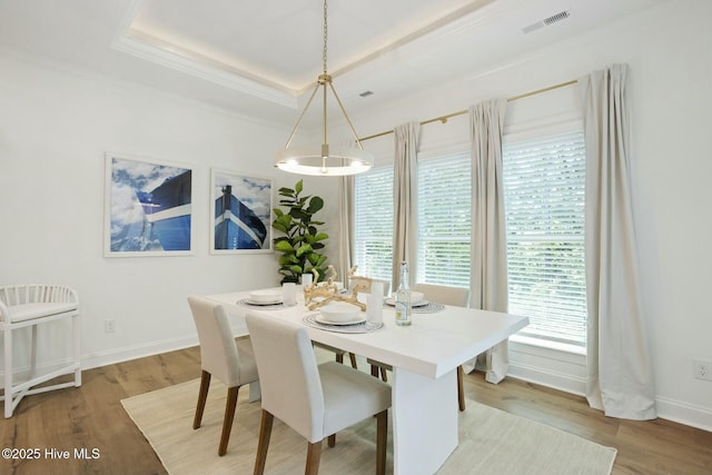 dining space featuring light hardwood / wood-style floors, ornamental molding, and a raised ceiling