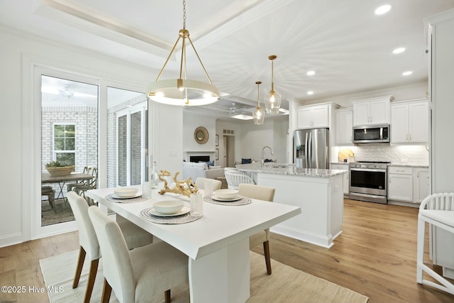 dining space featuring sink, light hardwood / wood-style floors, ornamental molding, and a tray ceiling