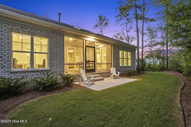 back house at dusk with a patio and a lawn