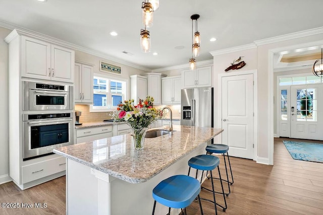 kitchen with appliances with stainless steel finishes, sink, white cabinetry, and a kitchen island with sink