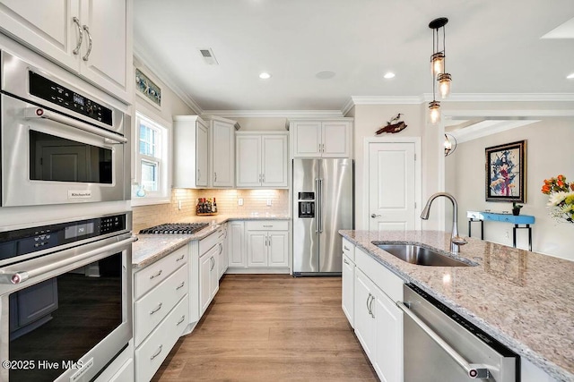 kitchen with stainless steel appliances, white cabinets, decorative light fixtures, and sink