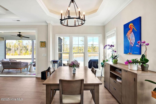 dining area with crown molding, wood-type flooring, ceiling fan with notable chandelier, and a tray ceiling