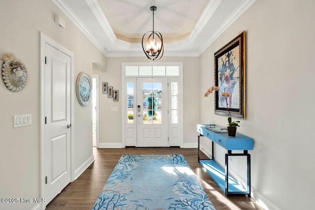 foyer with a raised ceiling, dark wood-type flooring, an inviting chandelier, and ornamental molding