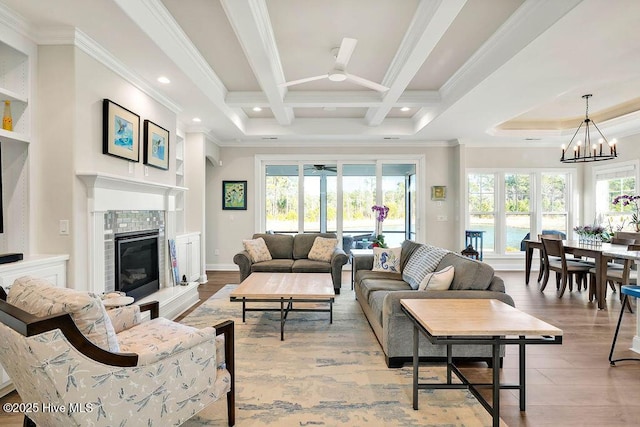 living room with crown molding, a tiled fireplace, beamed ceiling, and ceiling fan with notable chandelier