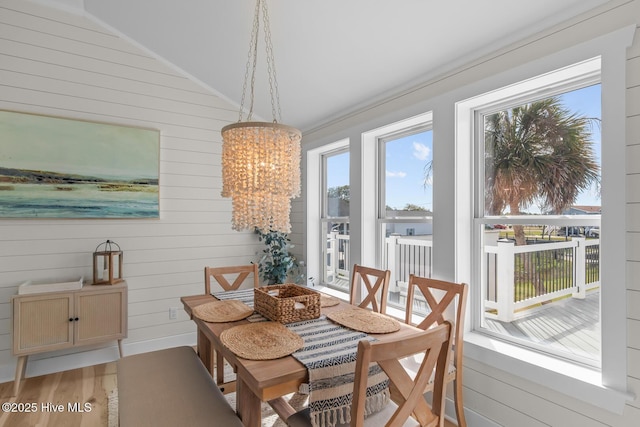 dining area with a notable chandelier, vaulted ceiling, wood walls, and light hardwood / wood-style flooring