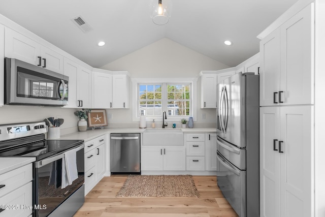 kitchen featuring appliances with stainless steel finishes, lofted ceiling, sink, white cabinets, and light wood-type flooring