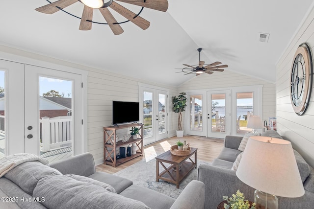 living room with lofted ceiling, wood walls, light hardwood / wood-style floors, and french doors