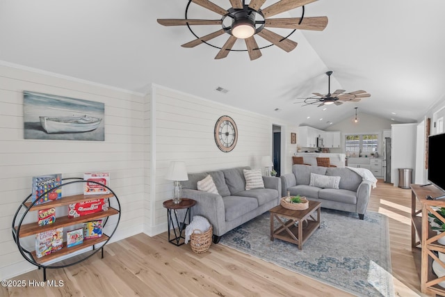 living room with ceiling fan, lofted ceiling, light hardwood / wood-style flooring, and wood walls