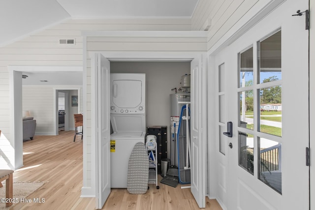 laundry room with hardwood / wood-style flooring, stacked washing maching and dryer, wood walls, and water heater