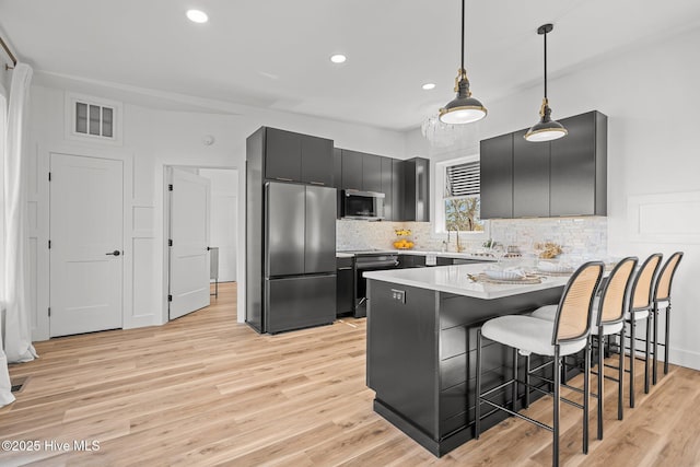 kitchen featuring hanging light fixtures, a breakfast bar area, stainless steel appliances, and light wood-type flooring