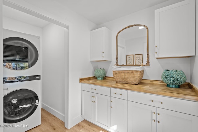 laundry room featuring cabinets, stacked washer / drying machine, and light hardwood / wood-style flooring