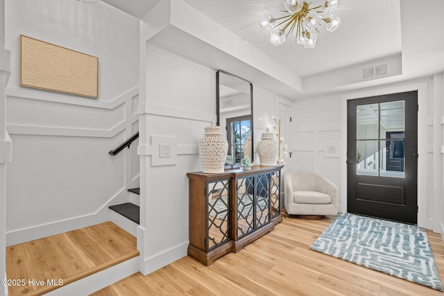 entrance foyer with hardwood / wood-style floors, an inviting chandelier, and a tray ceiling