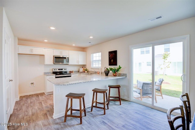 kitchen with stainless steel appliances, white cabinets, a kitchen bar, light hardwood / wood-style flooring, and kitchen peninsula