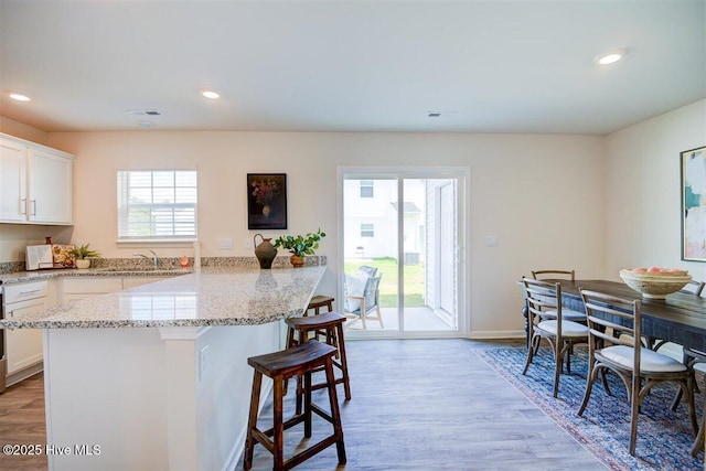 kitchen with white cabinets, a healthy amount of sunlight, a breakfast bar, and light stone countertops