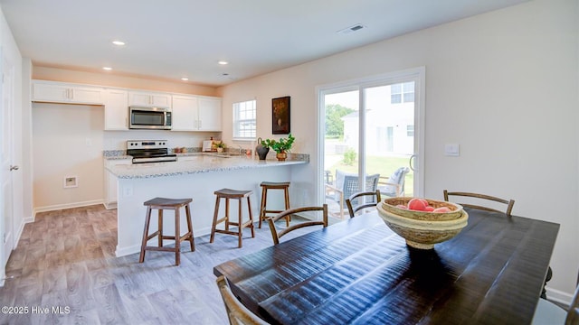 kitchen featuring kitchen peninsula, light wood-type flooring, a breakfast bar area, white cabinets, and appliances with stainless steel finishes