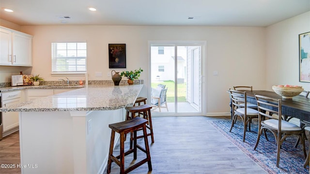 kitchen with light wood-style flooring, light stone countertops, a kitchen bar, white cabinetry, and recessed lighting