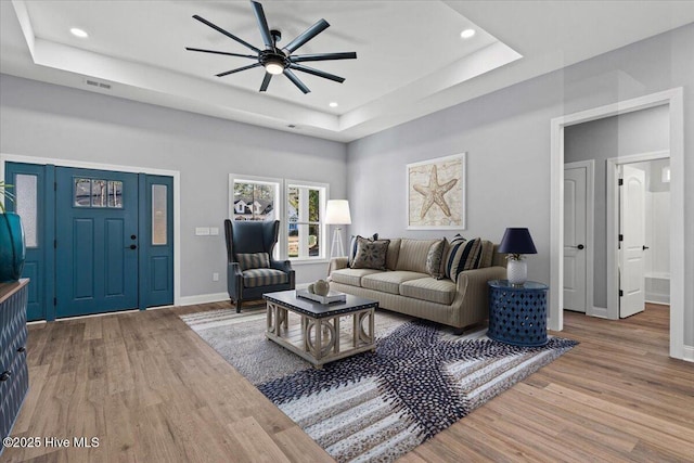 living room with a raised ceiling, ceiling fan, and light hardwood / wood-style flooring