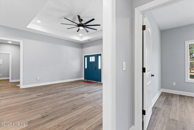 entrance foyer with ceiling fan, a raised ceiling, and light wood-type flooring