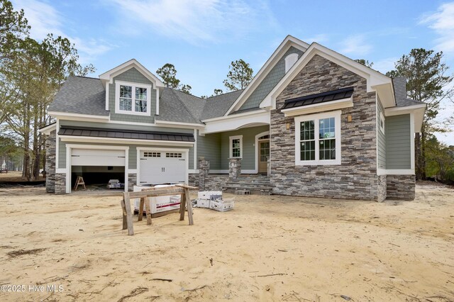 craftsman-style home featuring a standing seam roof, stone siding, roof with shingles, an attached garage, and metal roof