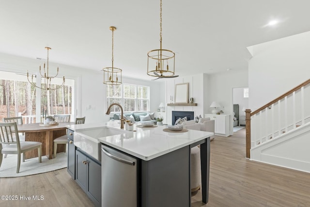 kitchen featuring dishwasher, pendant lighting, light hardwood / wood-style floors, a kitchen island with sink, and sink