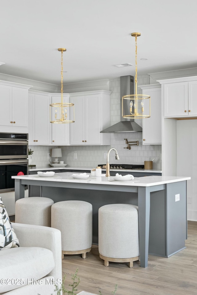 kitchen with decorative light fixtures, wall chimney range hood, and an island with sink