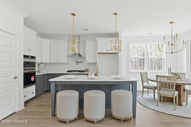 kitchen with white cabinets, wall chimney exhaust hood, a breakfast bar, pendant lighting, and gray cabinetry