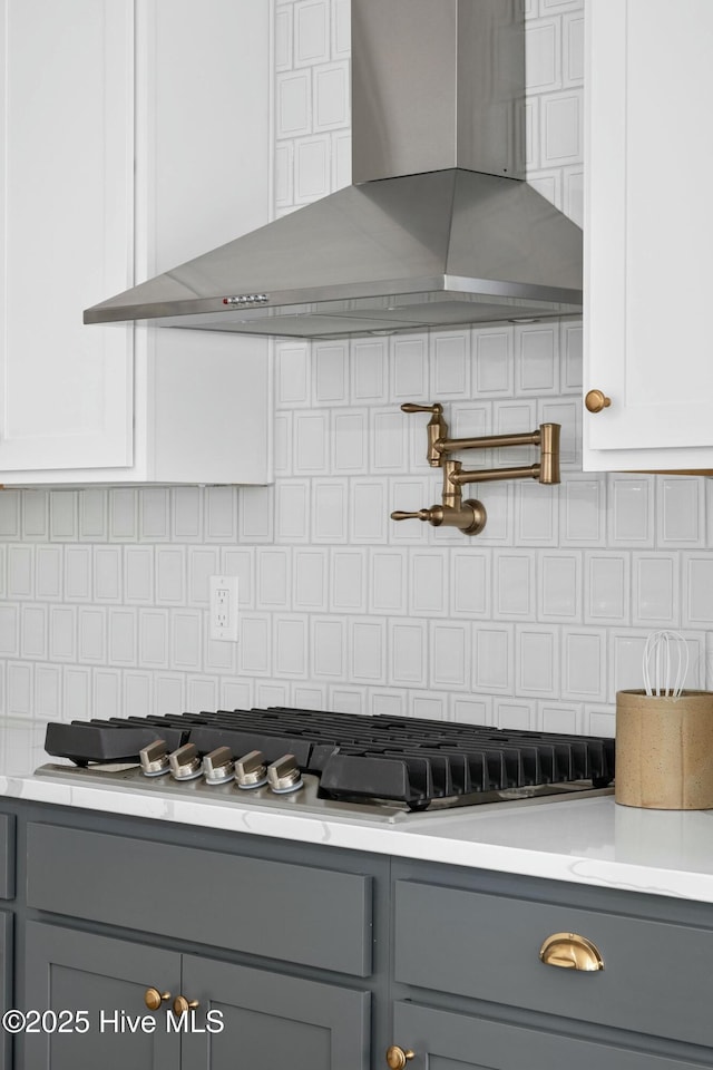 kitchen featuring white cabinets, wall chimney exhaust hood, gray cabinetry, and decorative backsplash