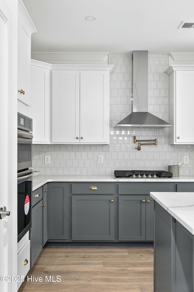 kitchen with stainless steel appliances, white cabinets, gray cabinetry, and wall chimney exhaust hood