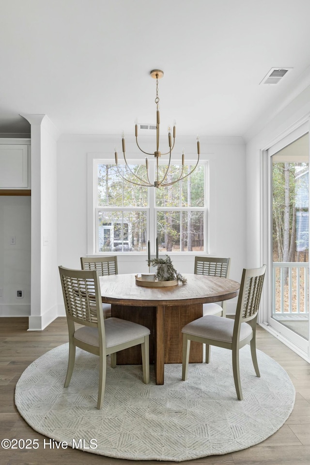 dining room with ornamental molding, an inviting chandelier, a wealth of natural light, and wood-type flooring