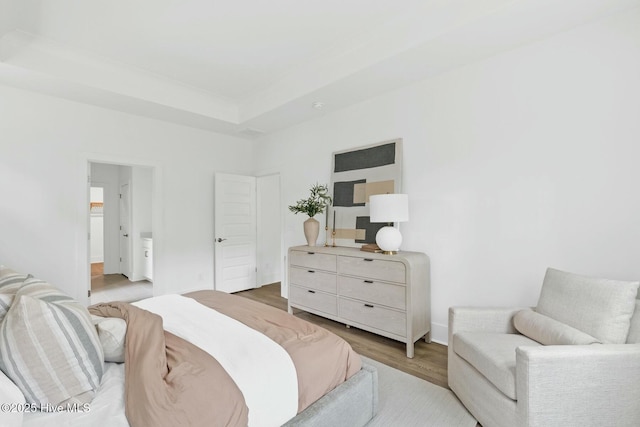 bedroom with ensuite bath, a tray ceiling, and light hardwood / wood-style flooring