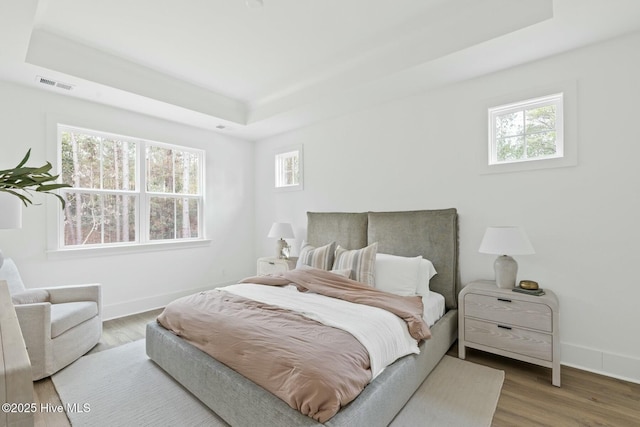 bedroom featuring wood-type flooring, multiple windows, and a tray ceiling