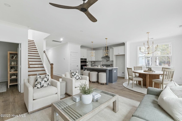 living room with ceiling fan with notable chandelier, sink, and light wood-type flooring