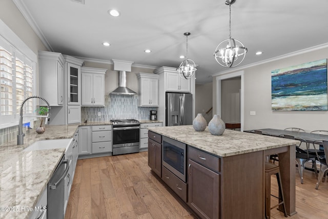 kitchen featuring light wood-style flooring, stainless steel appliances, a breakfast bar, a sink, and wall chimney exhaust hood