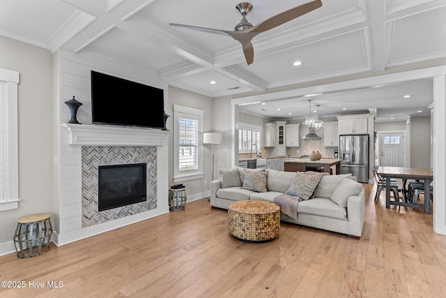 living area featuring a tiled fireplace, light wood finished floors, coffered ceiling, and ornamental molding