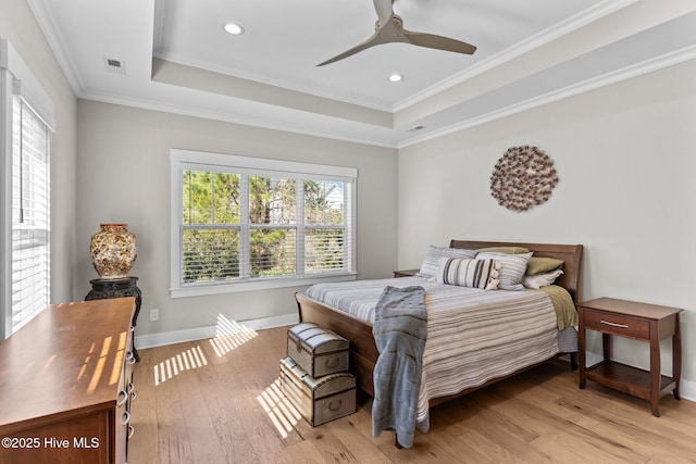 bedroom featuring a tray ceiling, light wood-style flooring, visible vents, and baseboards