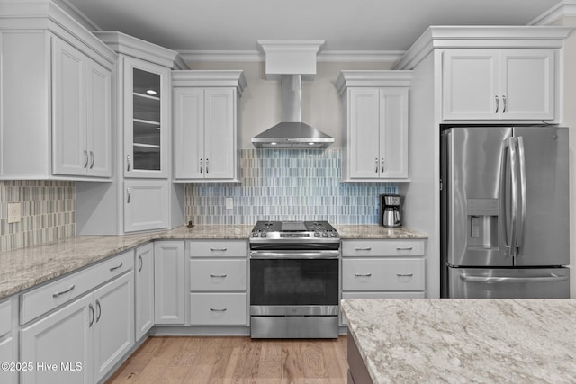 kitchen with light wood-style floors, appliances with stainless steel finishes, wall chimney exhaust hood, tasteful backsplash, and crown molding