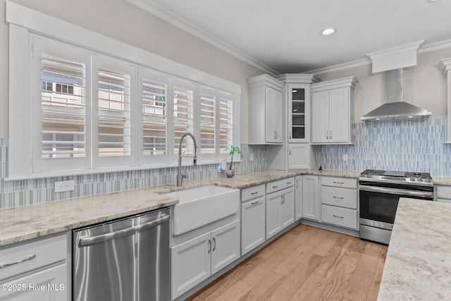 kitchen with a sink, appliances with stainless steel finishes, wall chimney range hood, and ornamental molding