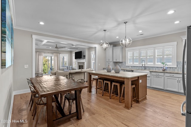 dining room featuring ceiling fan, recessed lighting, a fireplace, ornamental molding, and light wood finished floors