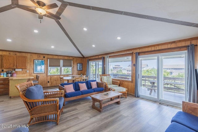 living room with vaulted ceiling, ceiling fan, light wood-type flooring, and wooden walls