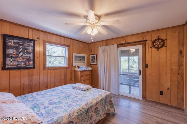 bedroom with ceiling fan, access to exterior, wood walls, and light wood-type flooring