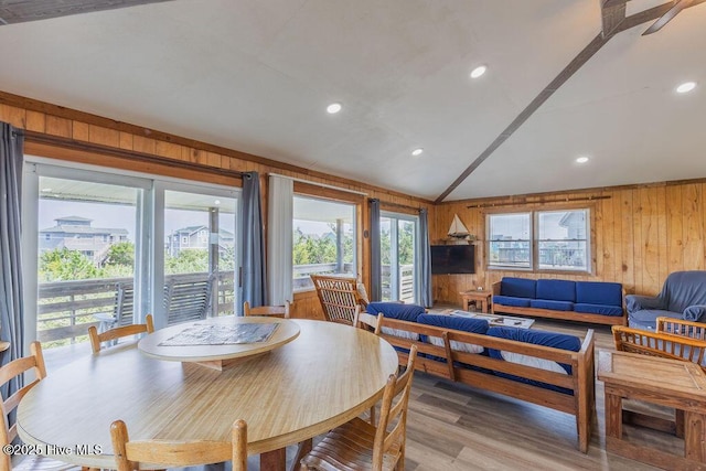 dining room featuring vaulted ceiling, a wealth of natural light, and wooden walls