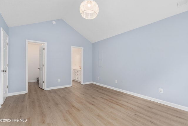 unfurnished bedroom with a closet, ensuite bath, light wood-type flooring, a spacious closet, and lofted ceiling