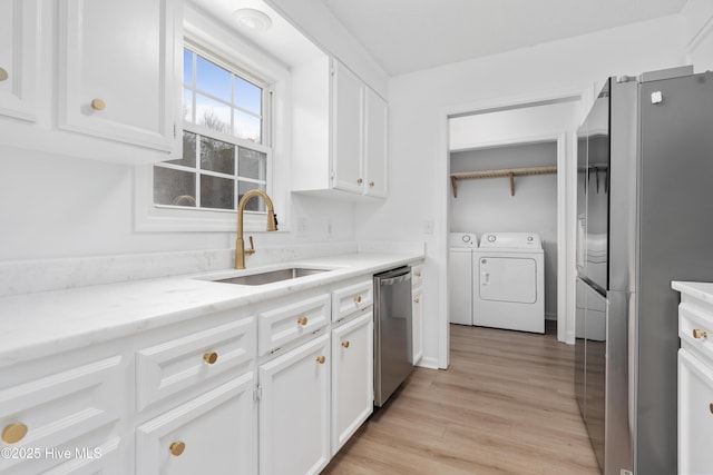 kitchen featuring stainless steel appliances, light wood-type flooring, white cabinets, washer and dryer, and sink