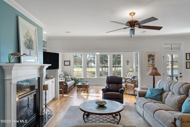 living room with a high end fireplace, a wealth of natural light, ornamental molding, and light hardwood / wood-style floors