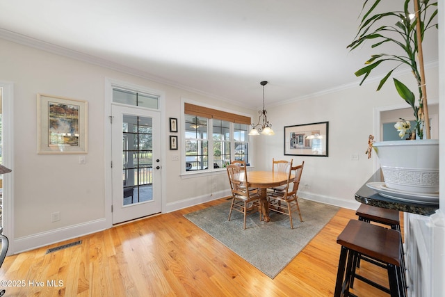 dining room featuring light wood-type flooring, ornamental molding, and a notable chandelier