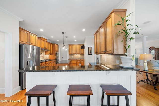 kitchen featuring pendant lighting, kitchen peninsula, light wood-type flooring, ornamental molding, and dark stone counters