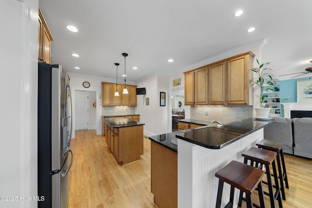 kitchen featuring pendant lighting, kitchen peninsula, light wood-type flooring, a breakfast bar area, and stainless steel fridge