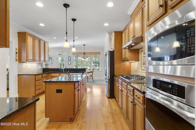 kitchen with pendant lighting, appliances with stainless steel finishes, a kitchen island, dark stone countertops, and crown molding